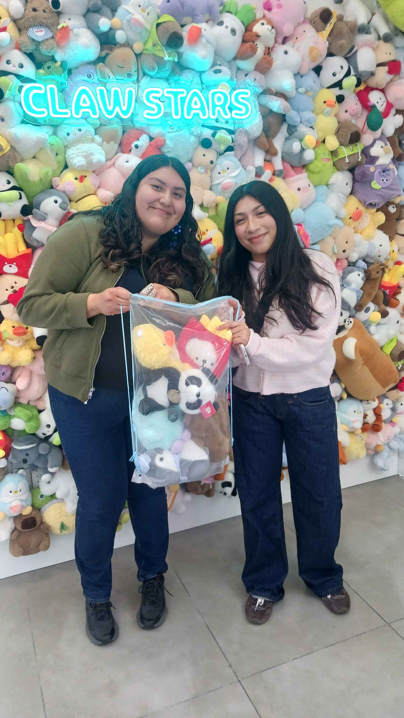 Two friends holding a bag bursting with plushies they won at Claw Stars